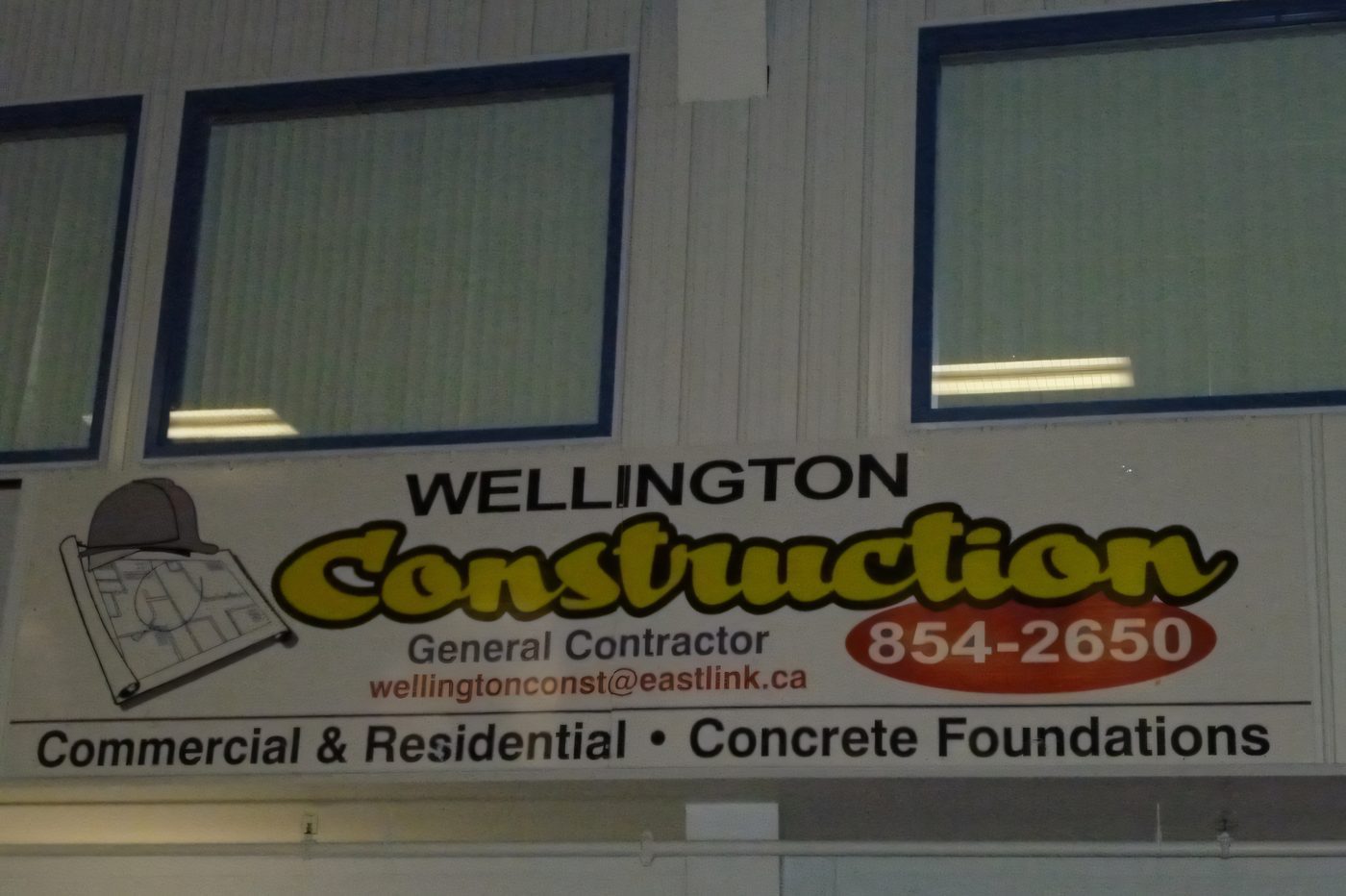 A Wellington Construction sponsorship banner on the wall of a fitness room, listing commercial and residential work and concrete foundations