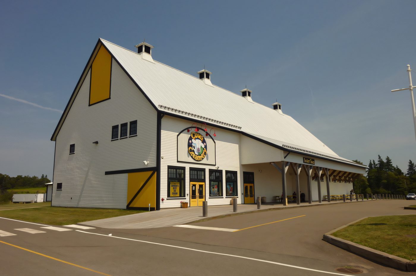 A white gambrel-roofed retail building with yellow trim, a full parking lot in front on a sunny day