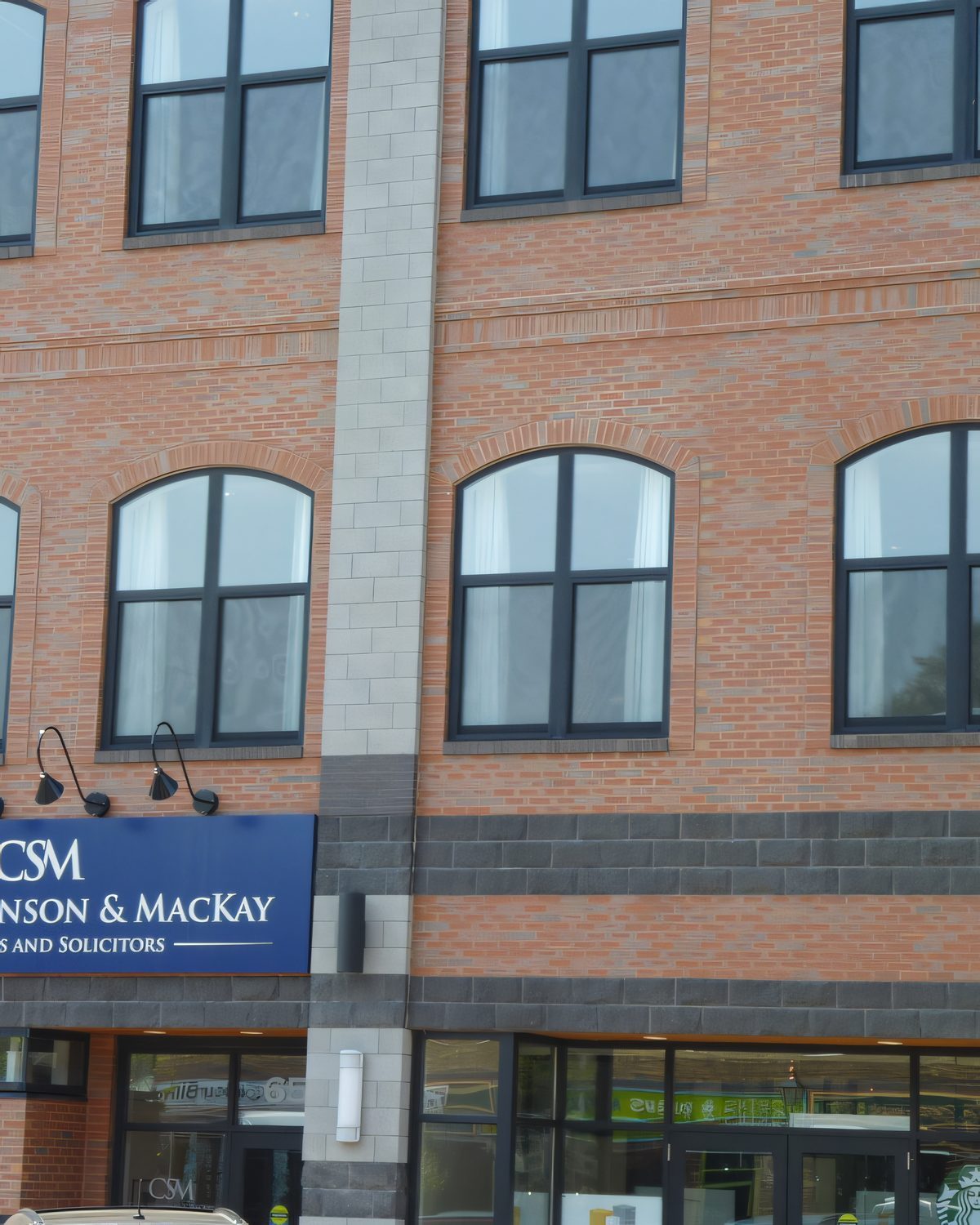 Close view of a three-storey brick office block with arched windows and a blue sign over the door