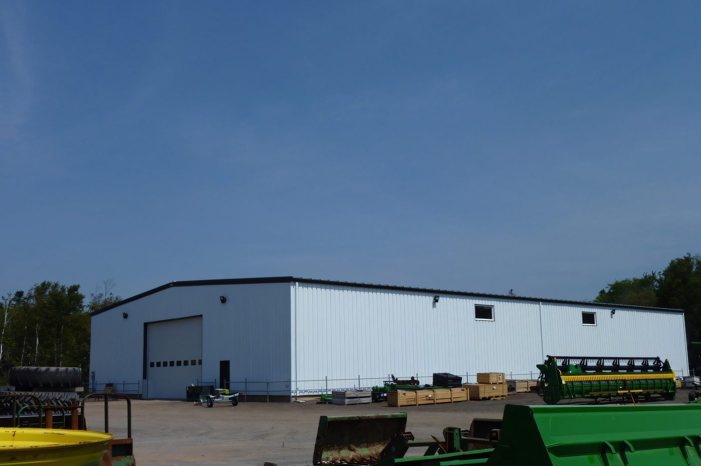 A white steel storage building with a wide door, farm equipment lined up in front