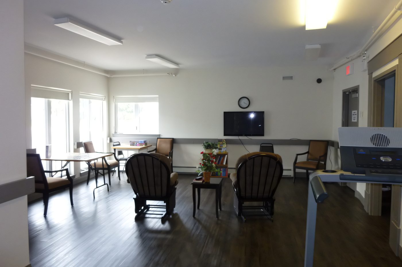 A bright common room with hardwood floors, armchairs and a wall-mounted television