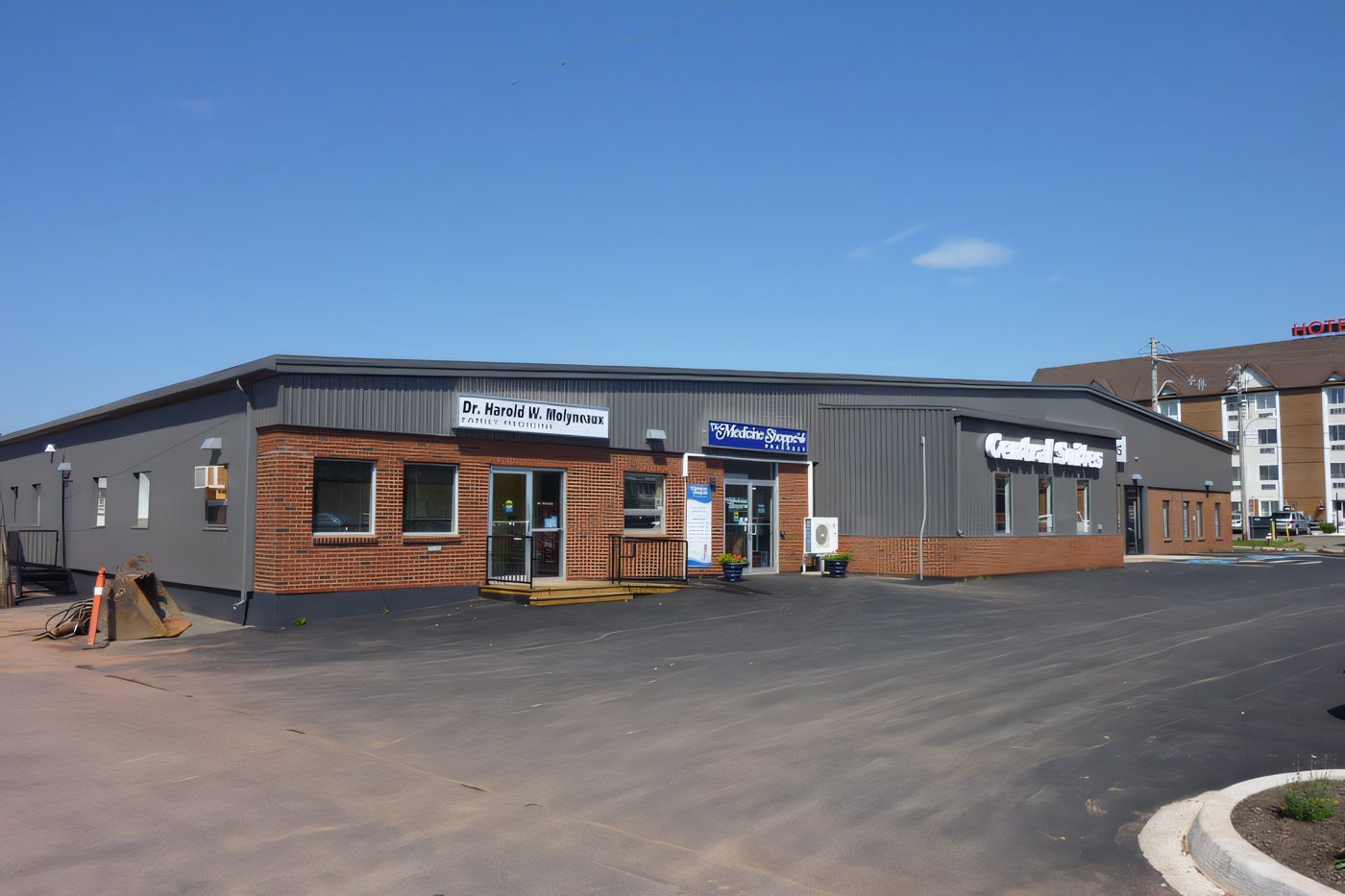 A brick and steel retail strip with tenant signs and a freshly paved parking lot