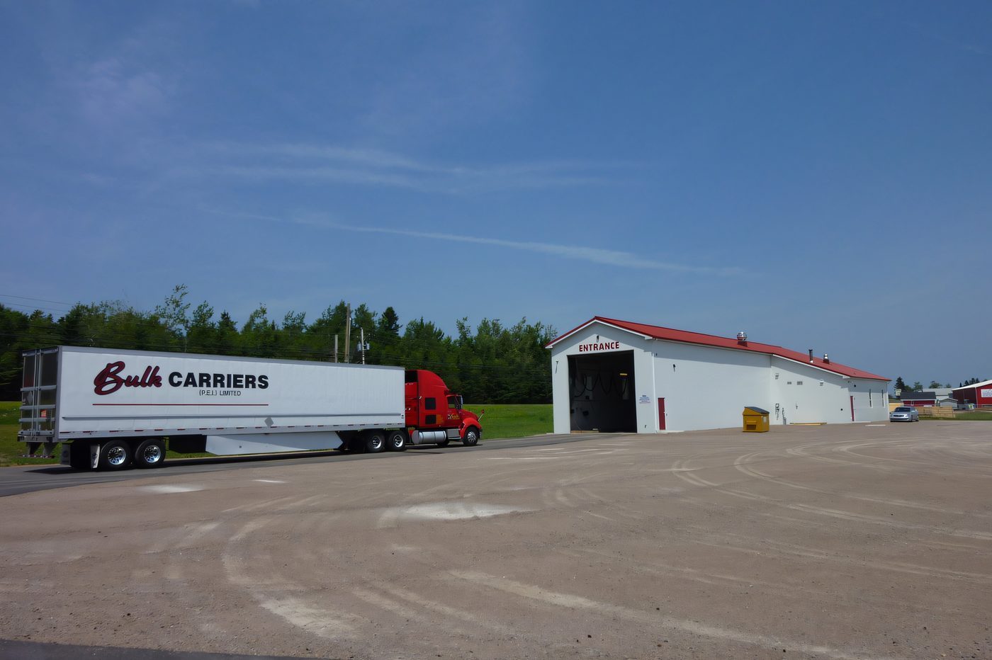 A transport trailer parked beside a white steel building with a red roof