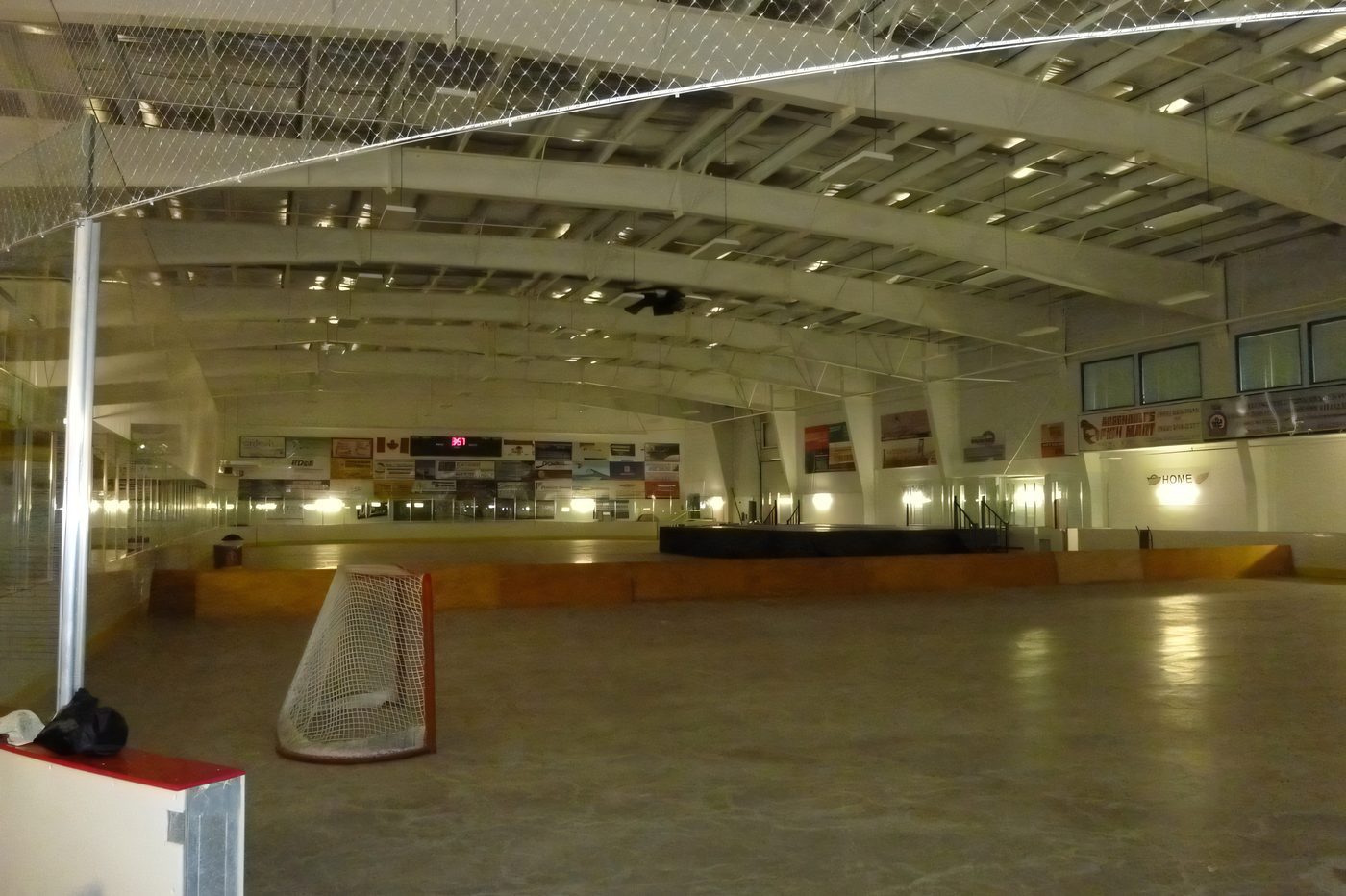 An empty arena floor under a clear-span steel roof, the nets and boards in place, lights on