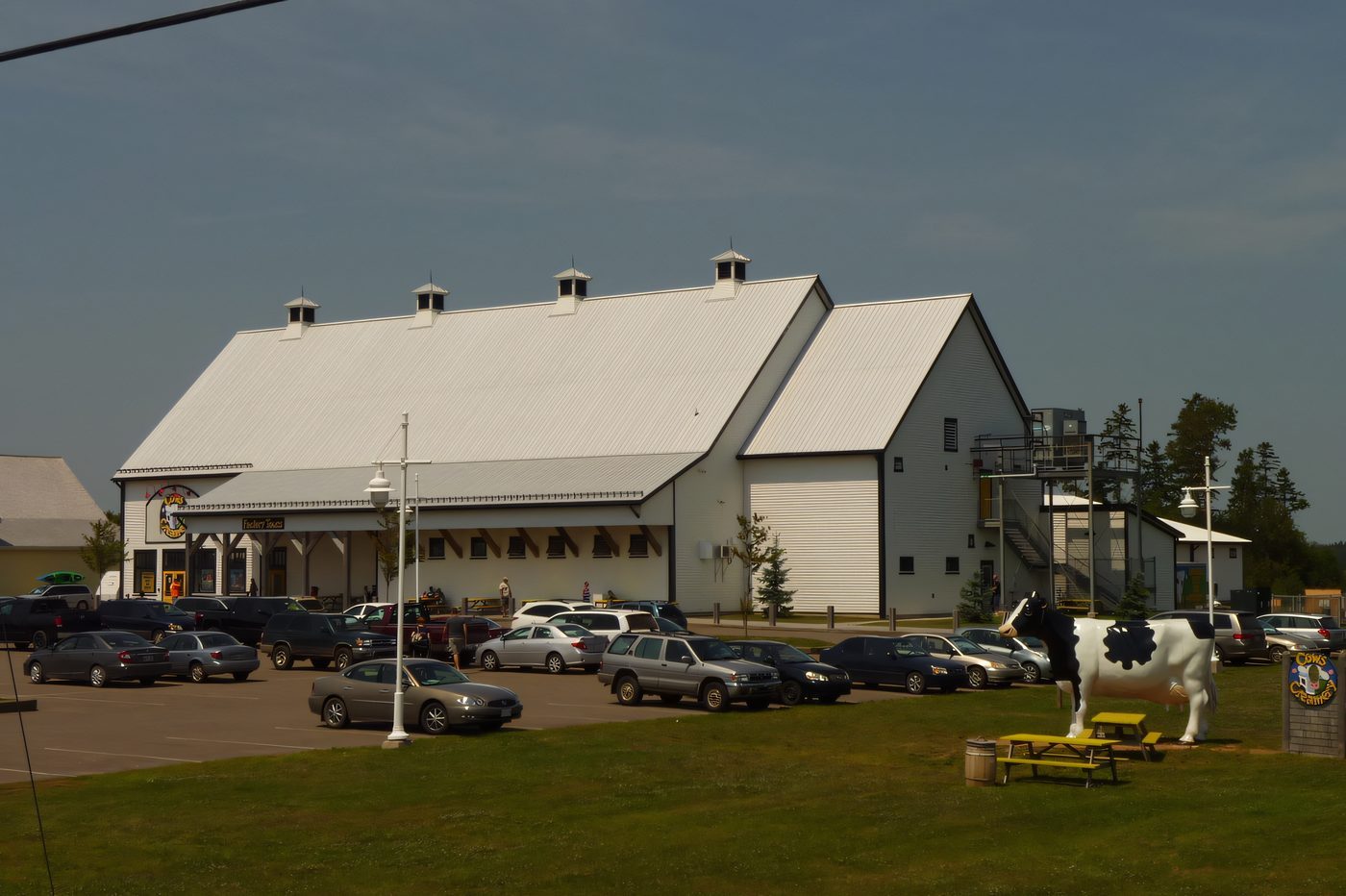 A large white gambrel-roofed retail building with yellow trim and a full parking lot