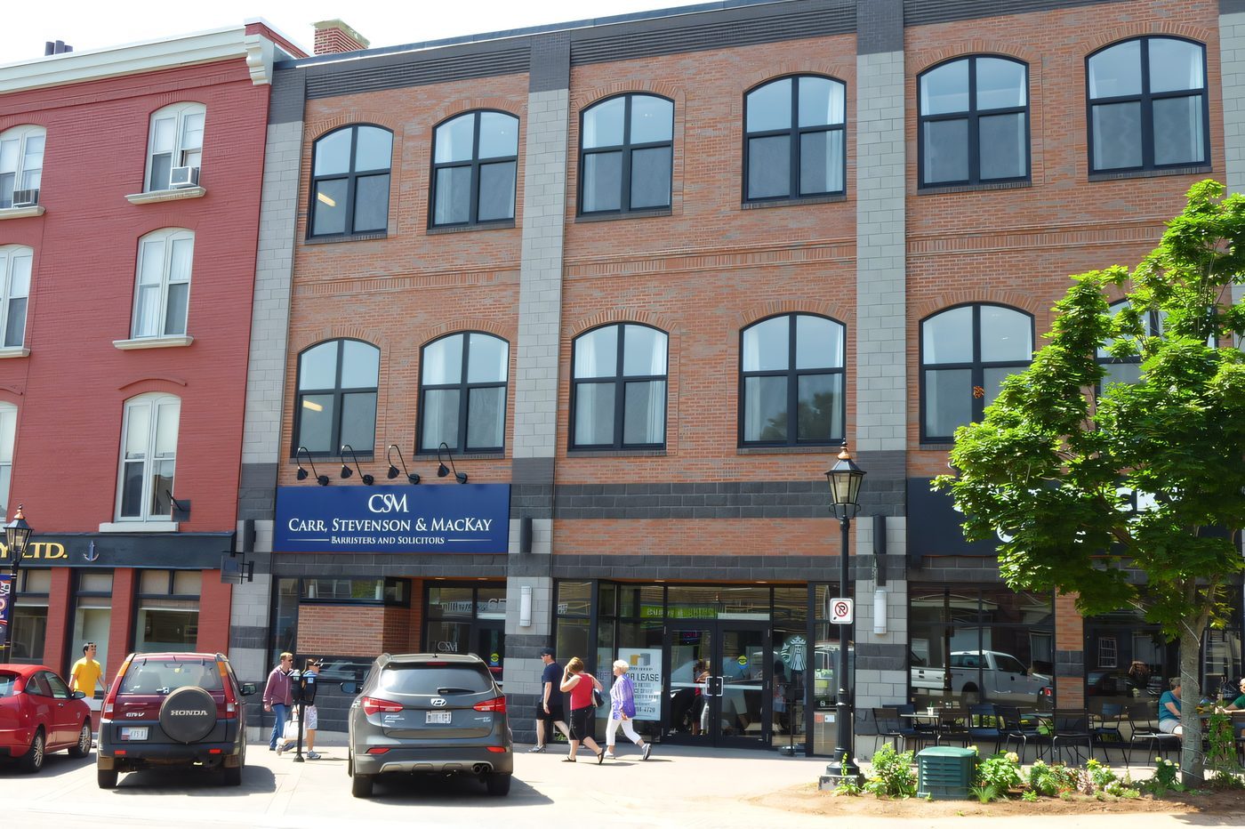 A three-storey brick and glass block on a busy downtown street, people on the sidewalk