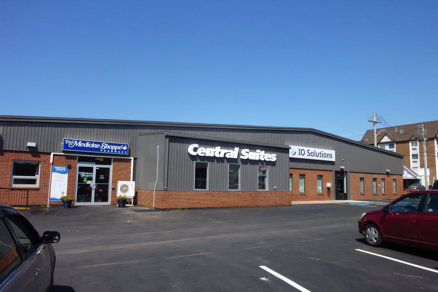 A brick and steel retail strip with several tenant signs and a fresh parking lot