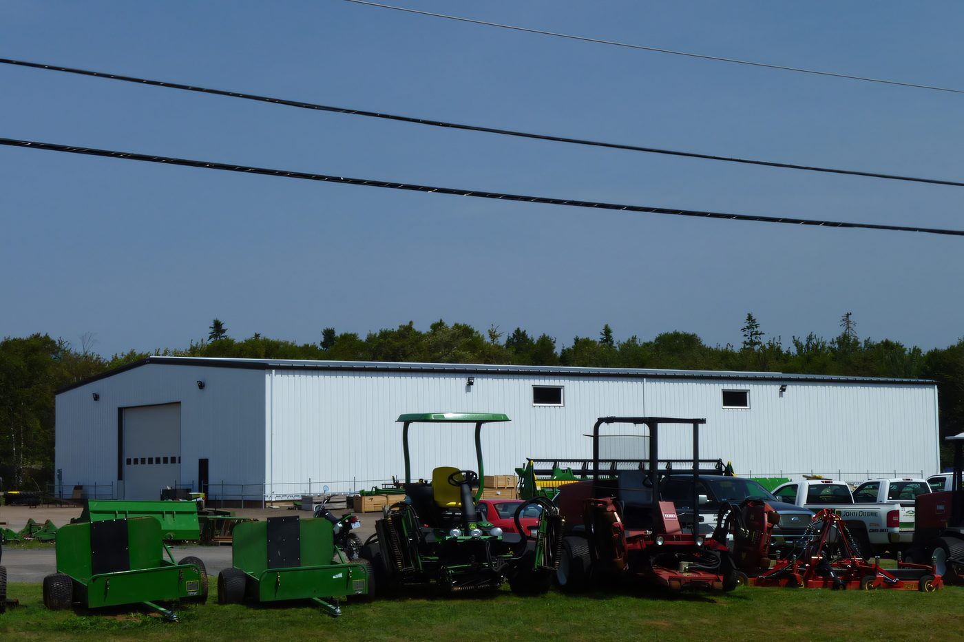 A white steel building with a wide bay door on a slab, tractors parked in front