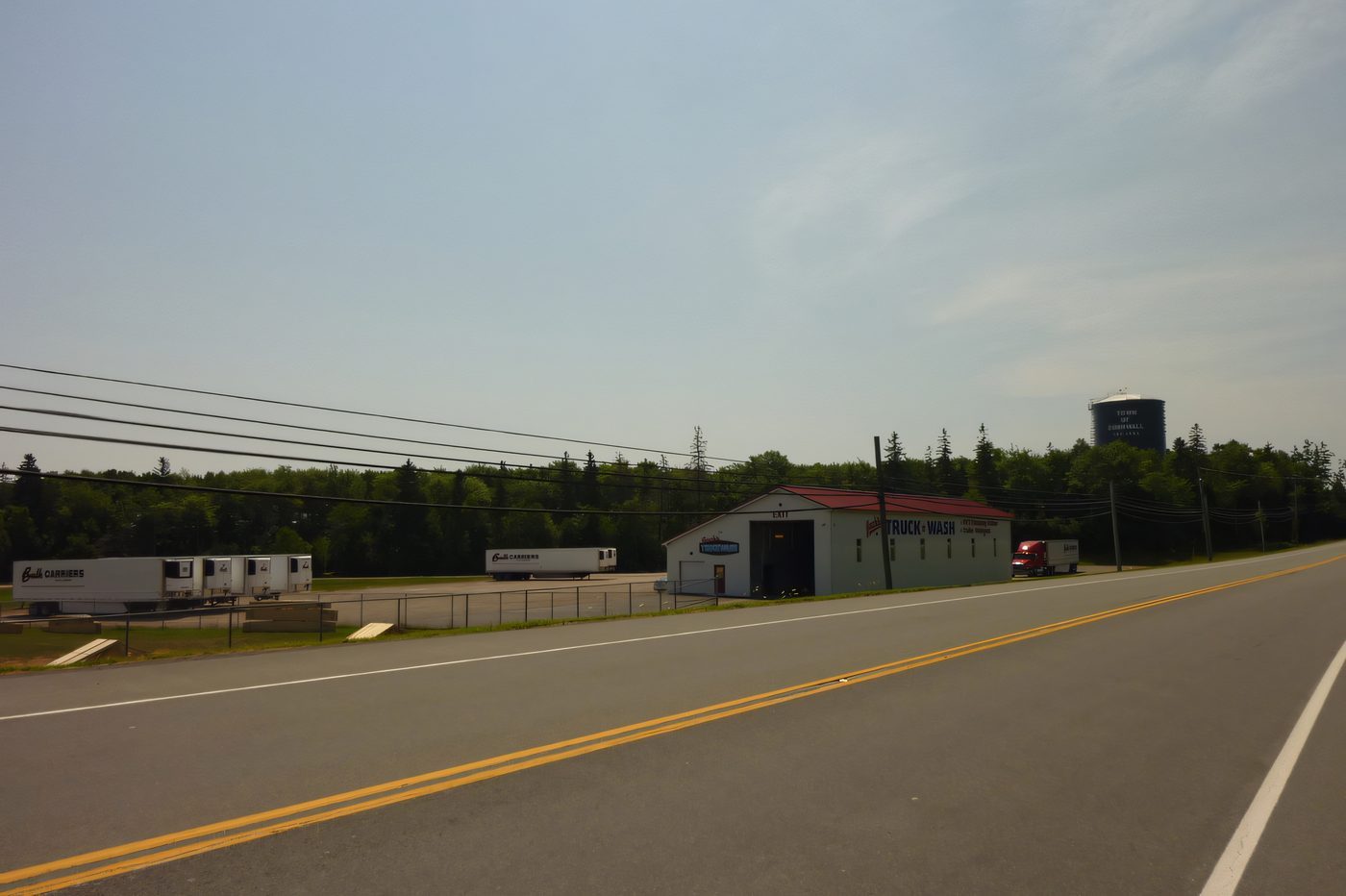 A red-roofed steel building set back from a country road, power lines overhead