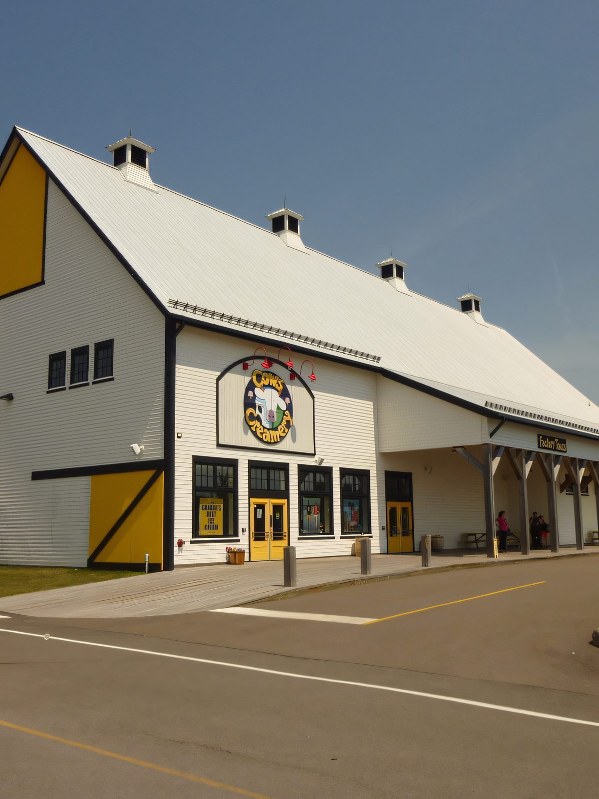 Side view of a white gambrel-roofed retail building with yellow trim, vent cupolas along the ridge