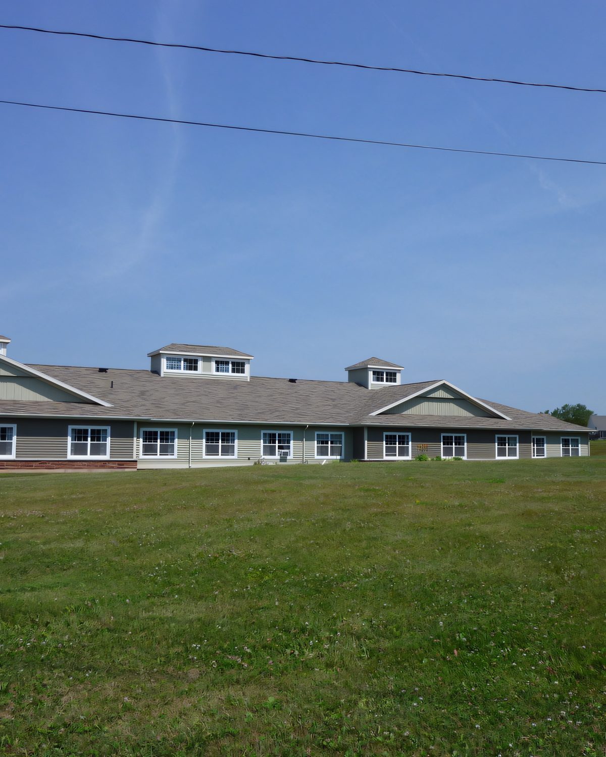 Cream-sided residential complex with dormers and a covered entry, seen across the lawn