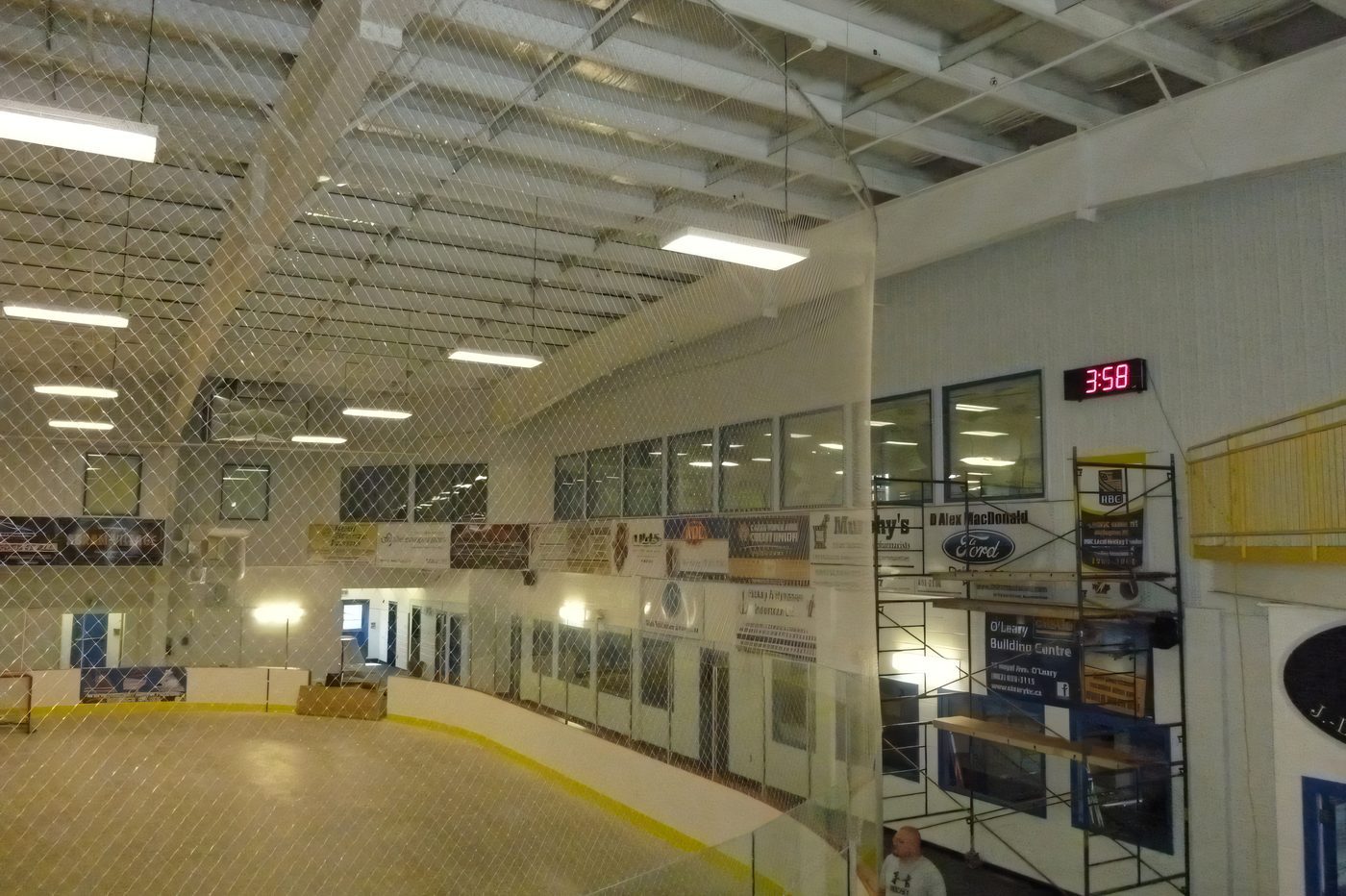 Inside an arena under construction, the steel roof structure and protective netting above the concrete floor