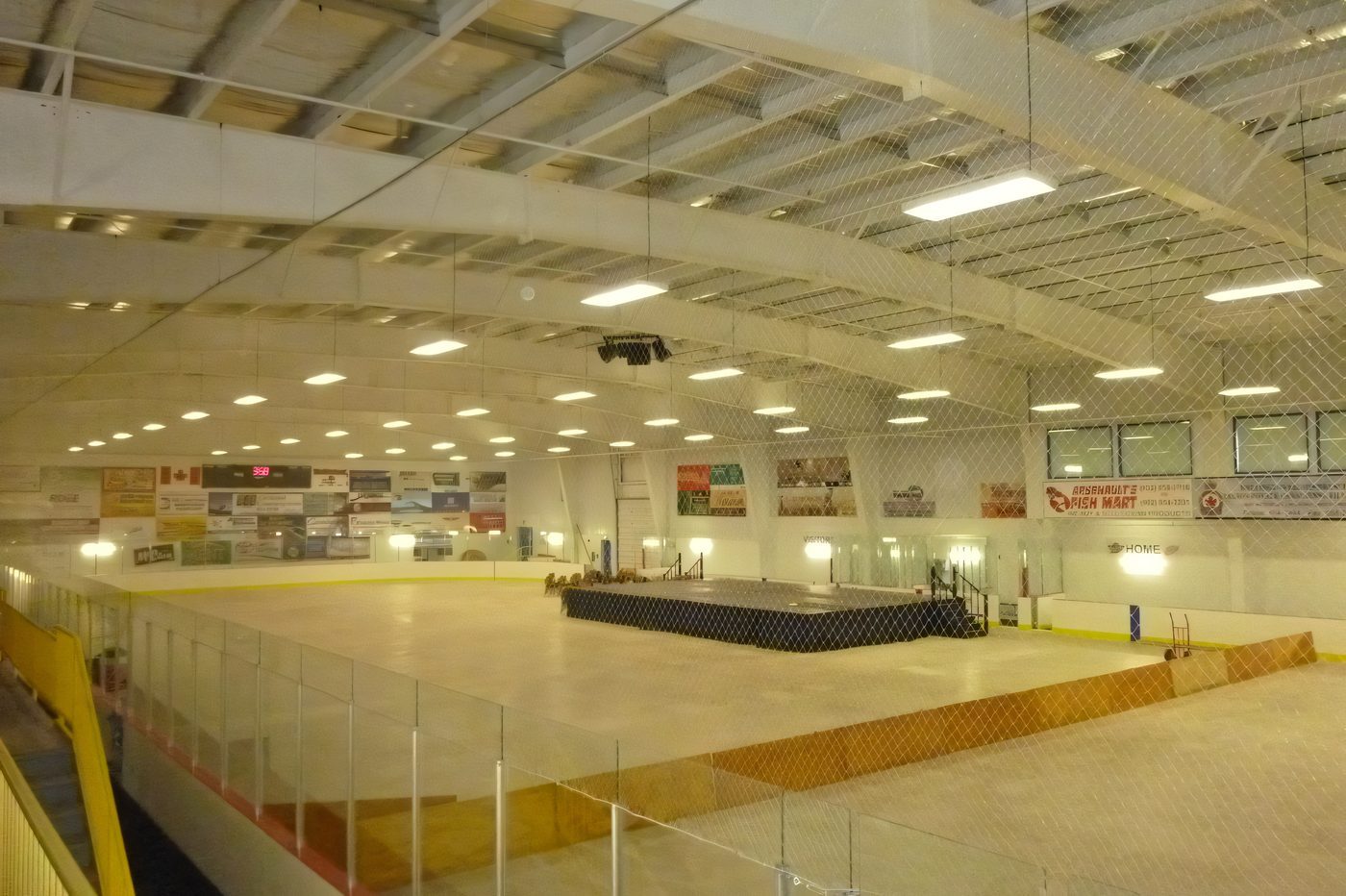 Rows of seats and yellow railings looking down on an arena ice surface, the steel roof above