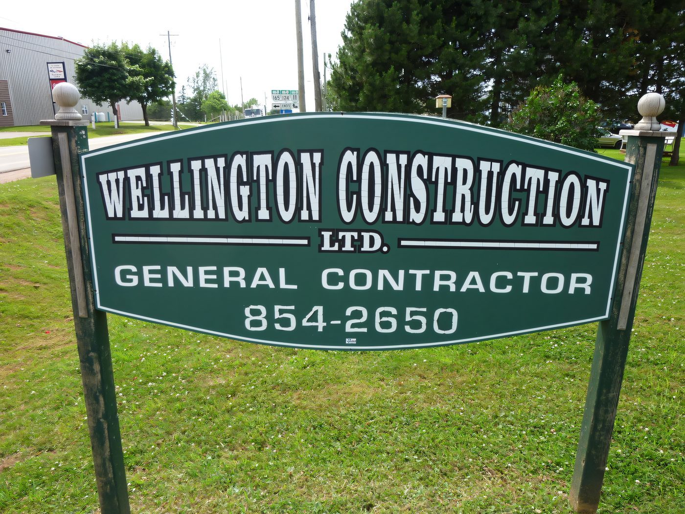 The green roadside sign reading Wellington Construction Ltd., General Contractor, 854-2650, standing on the lawn