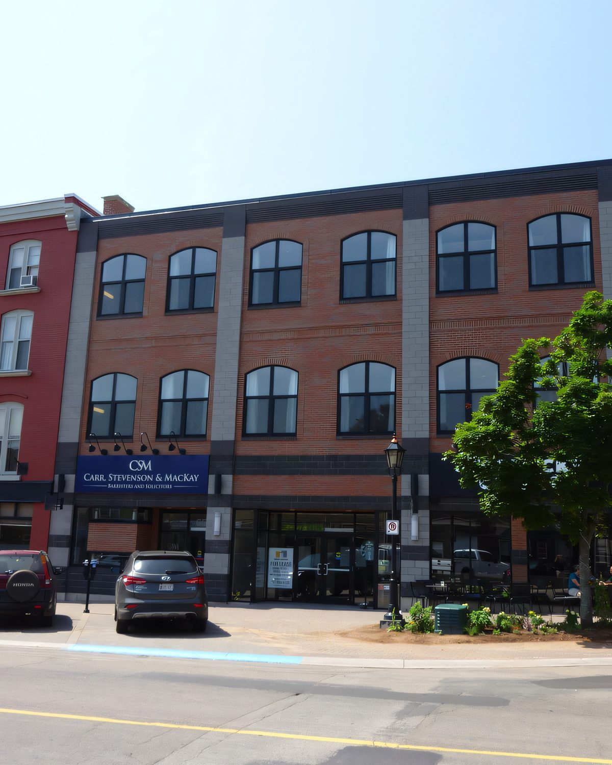 A three-storey brick and glass commercial block on a downtown street, lamp posts and parked cars in front