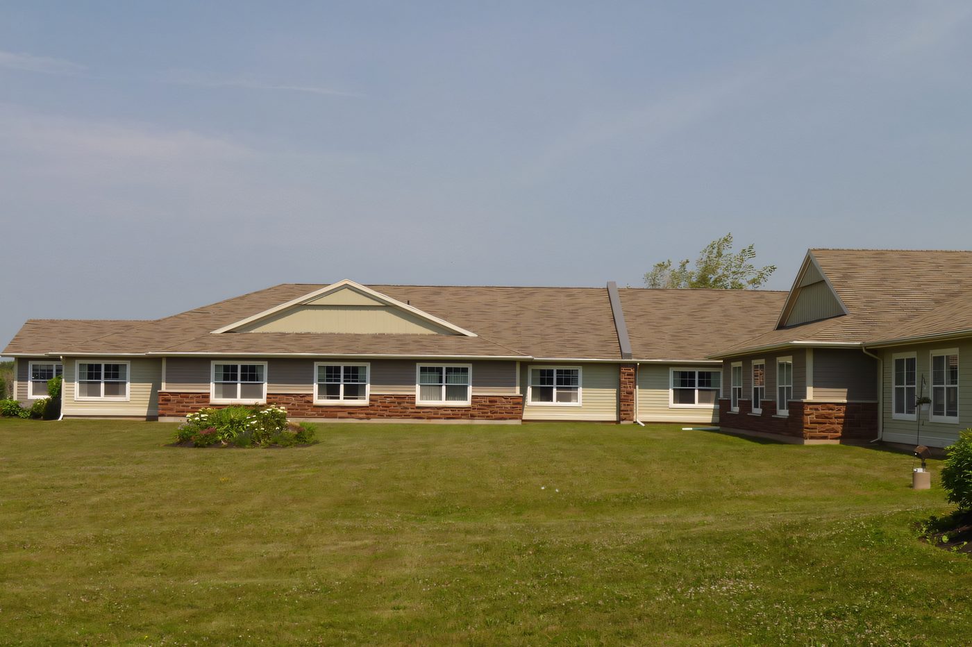 A single-storey residential complex with cream siding on a brick base, a lawn in front